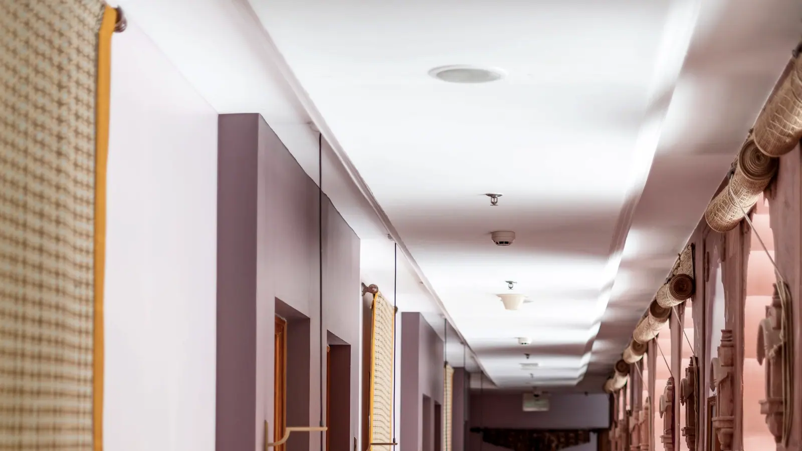 Hotel corridor lit low and warm by wall lamps at each door