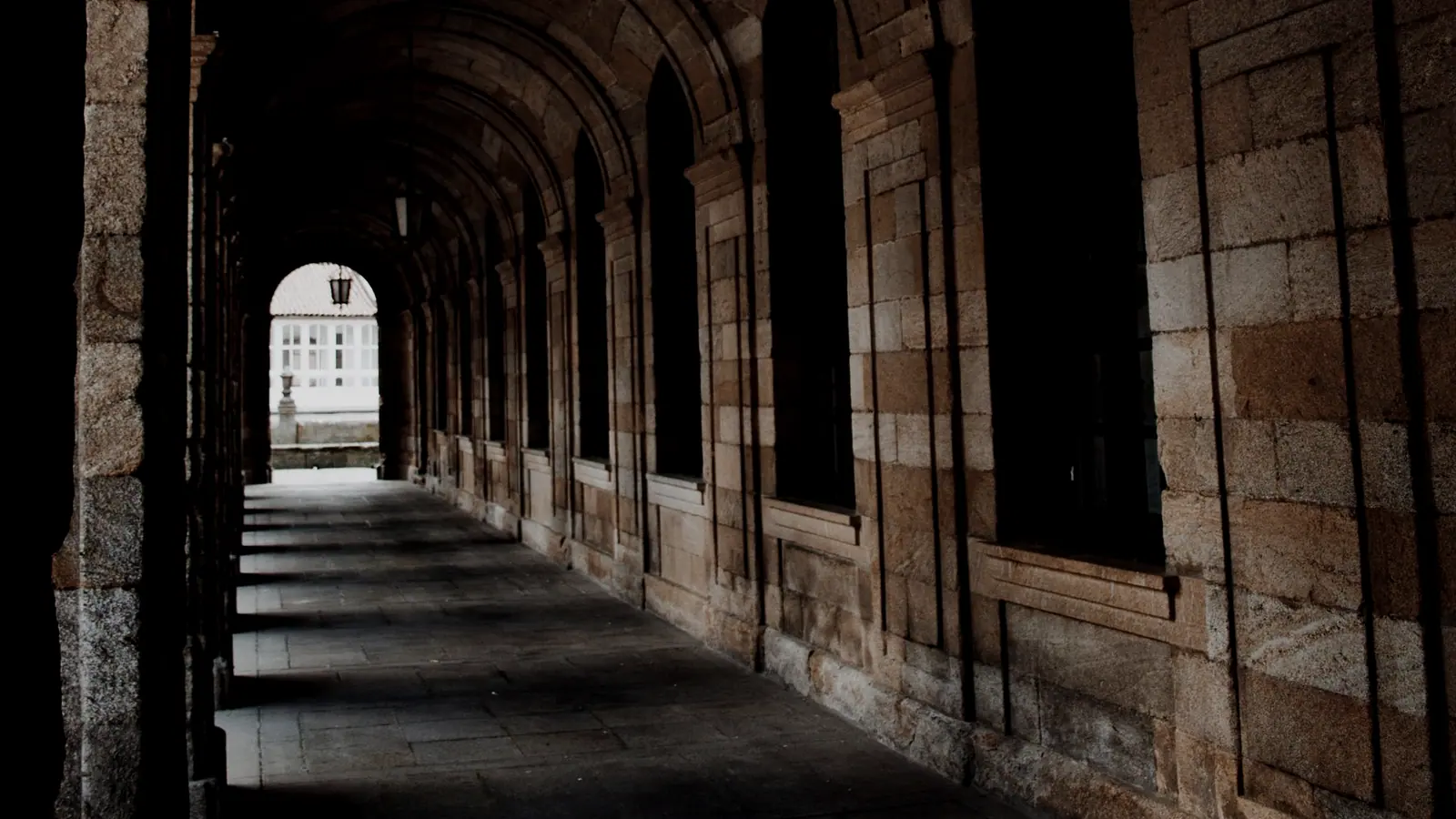 Dark vaulted stone arcade running toward a bright doorway