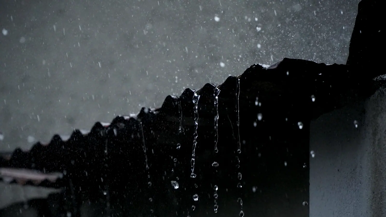 Rain falling in a sheet from the edge of a dark tiled roof