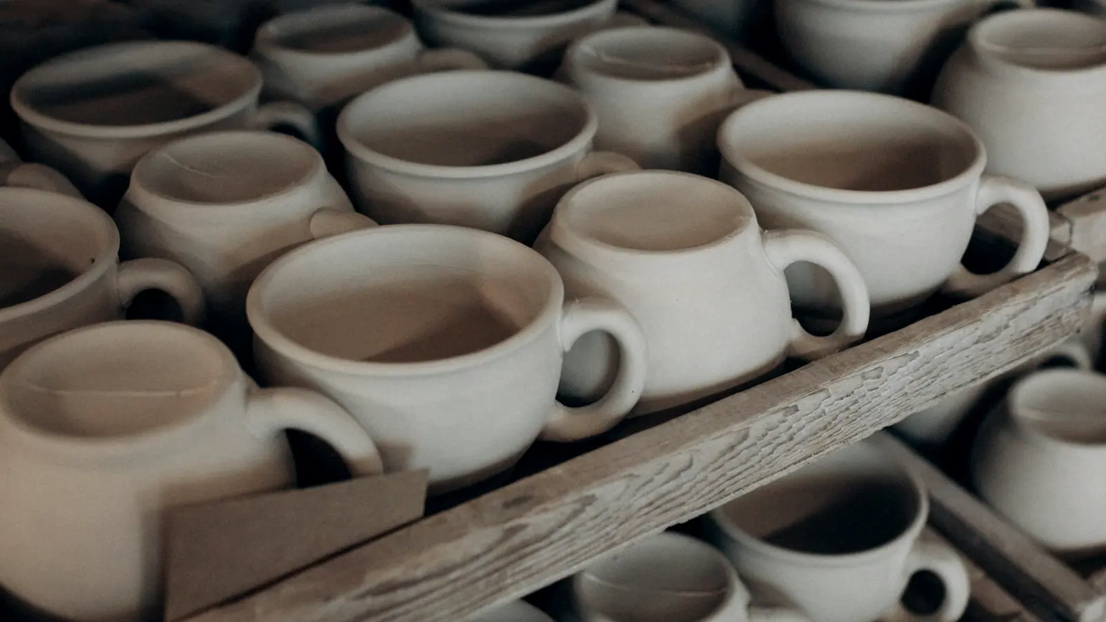 Rows of unfired stoneware vessels drying on a workshop shelf