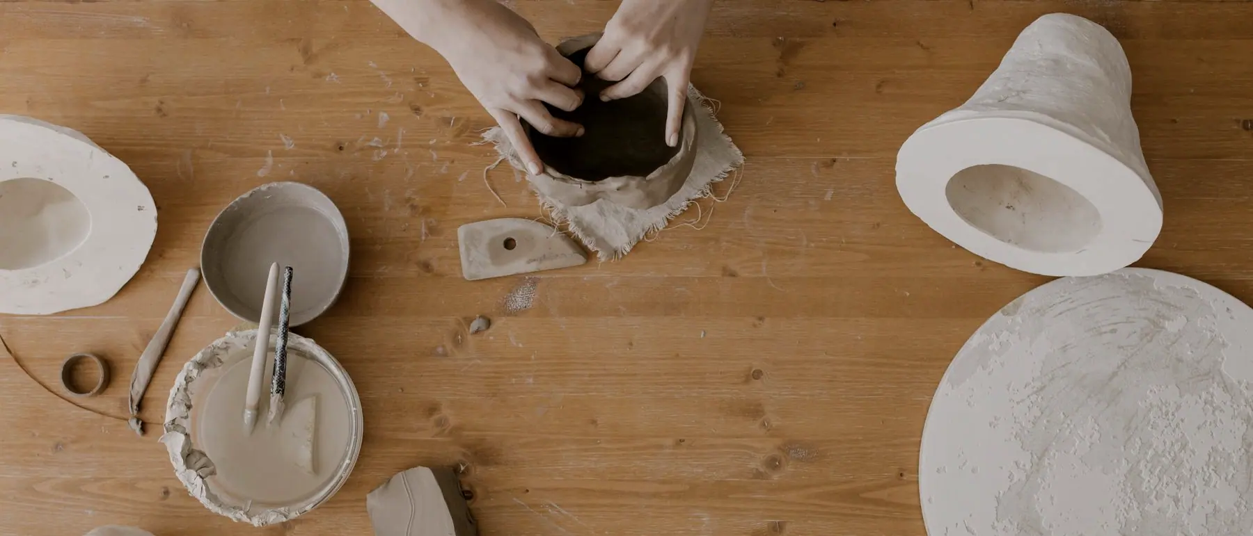 Hands forming a clay vessel wall on a timber bench